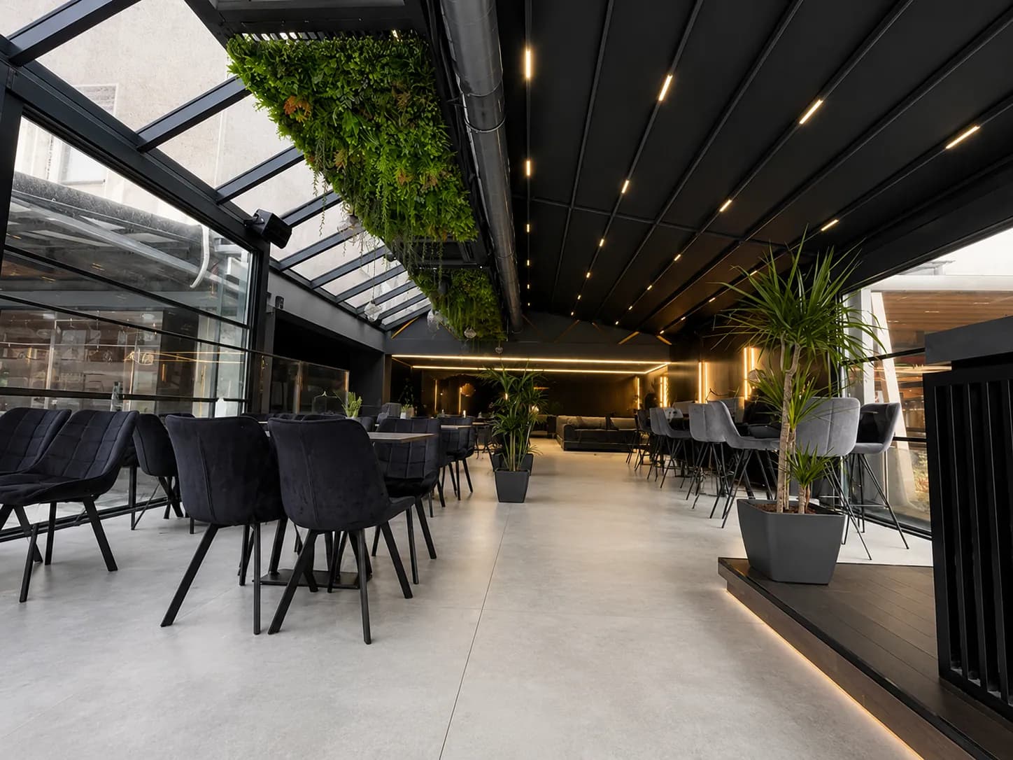 Gastronomie-Terrasse unter Lamellendach mit Pflanzenwand und Loungebestuhlung