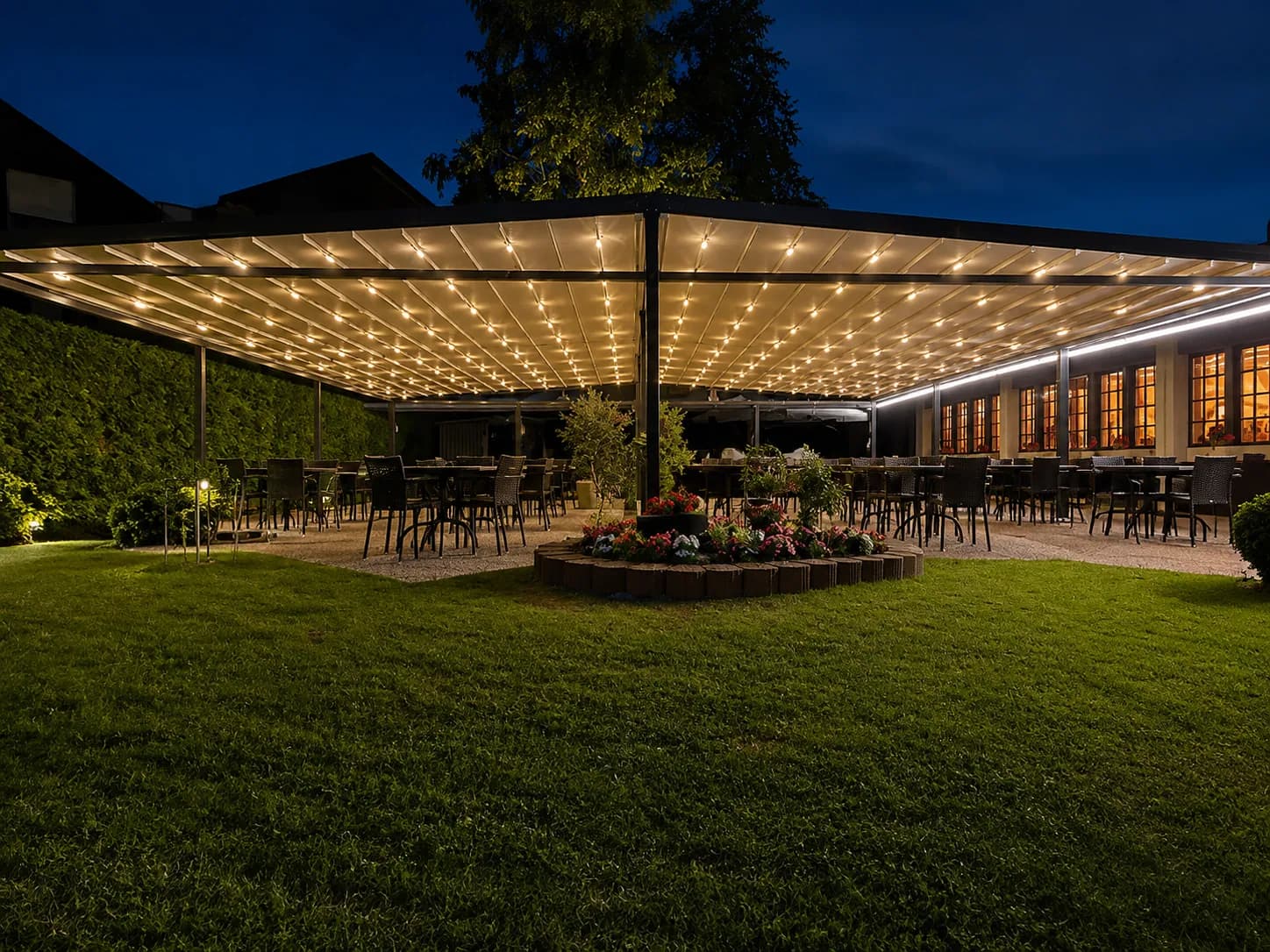 Beleuchtete Gastronomie-Pergola bei Nacht mit gedeckten Tischen im Garten