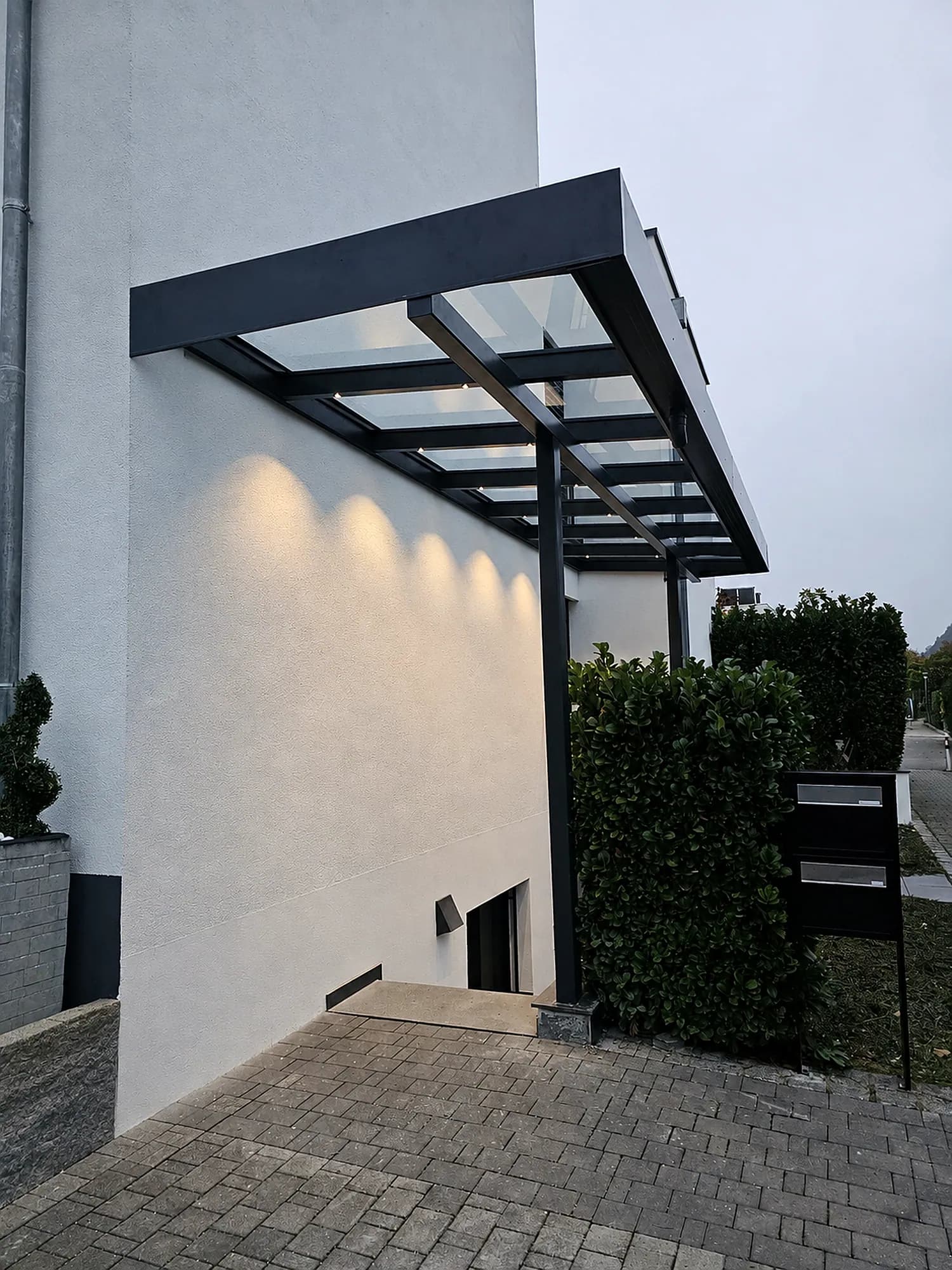 Vordach aus Glas und Aluminium über dem Eingang eines modernen weißen Hauses