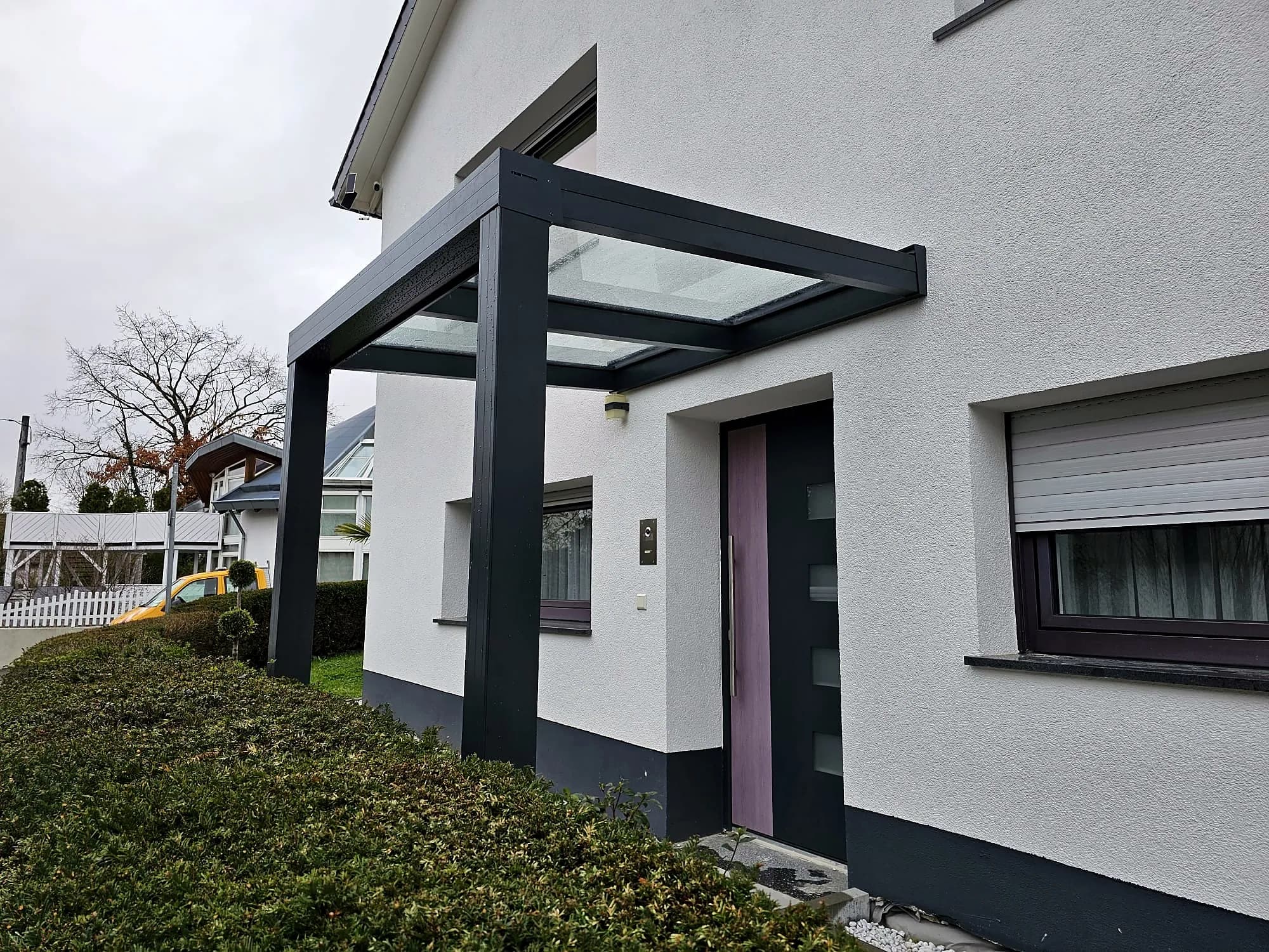 Vordach mit Glas über dem Hauseingang eines weißen Wohnhauses