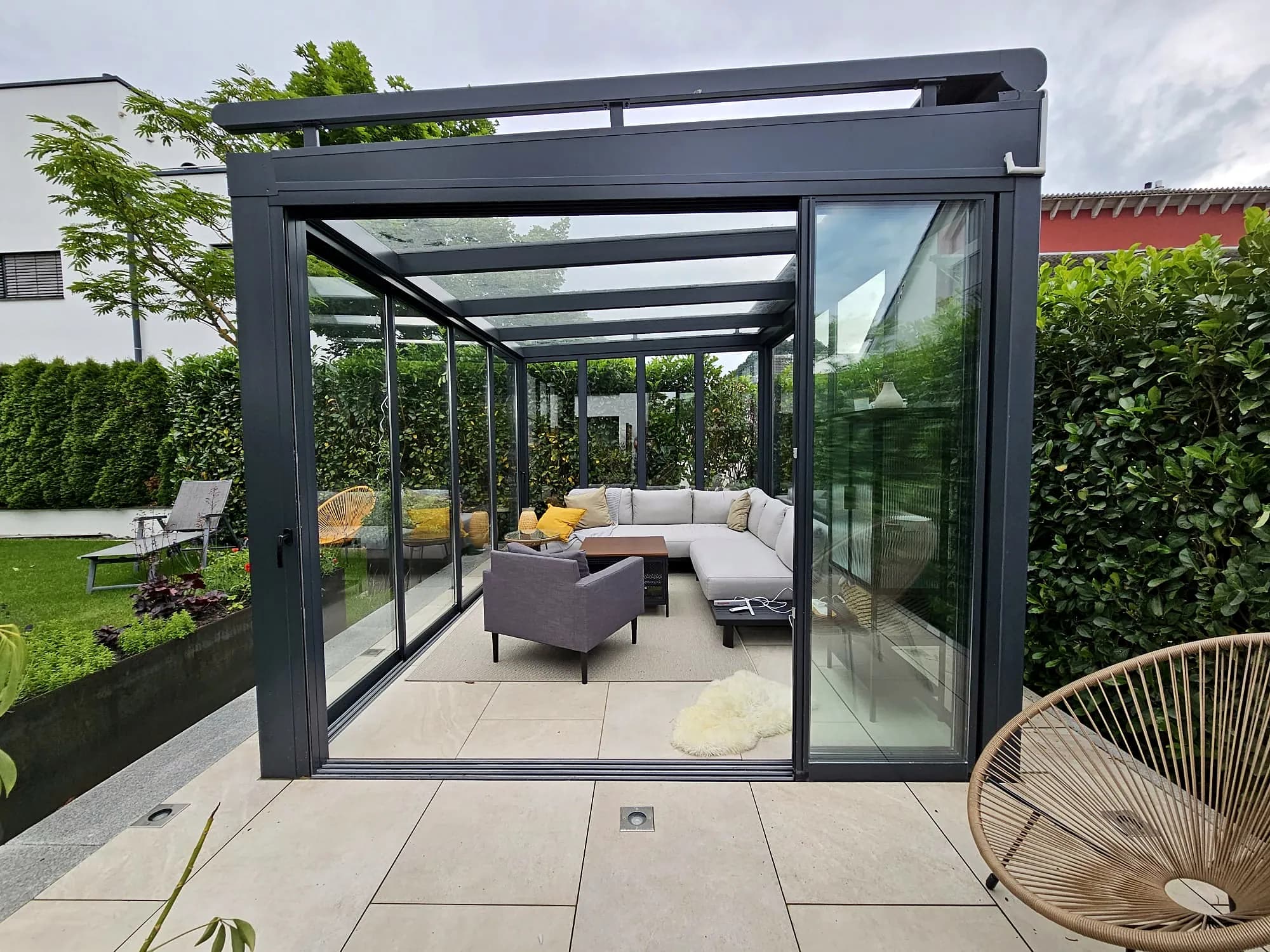 Glashaus im Garten mit geöffneter Schiebetür und heller Sitzlounge