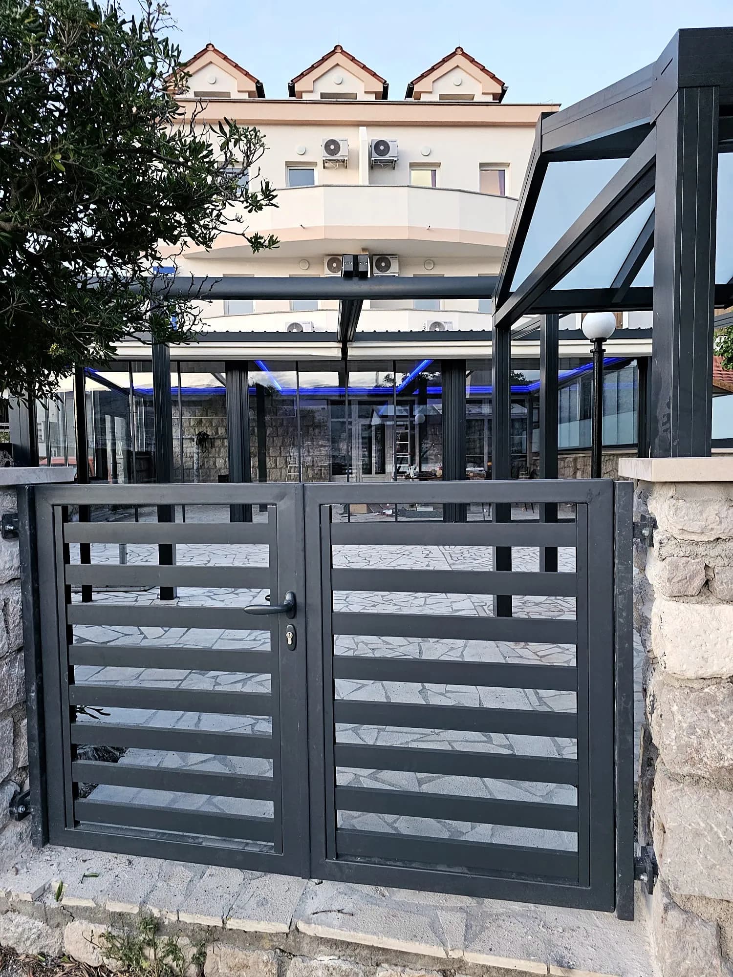 Gartentor aus Aluminium mit Natursteinmauer vor einem Hotel